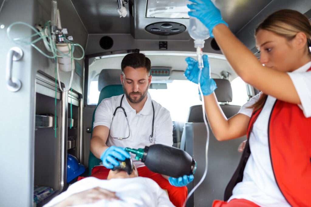 view from inside ambulance of uniformed emergency services workers caring for patient on stretcher during coronavirus pandemic.